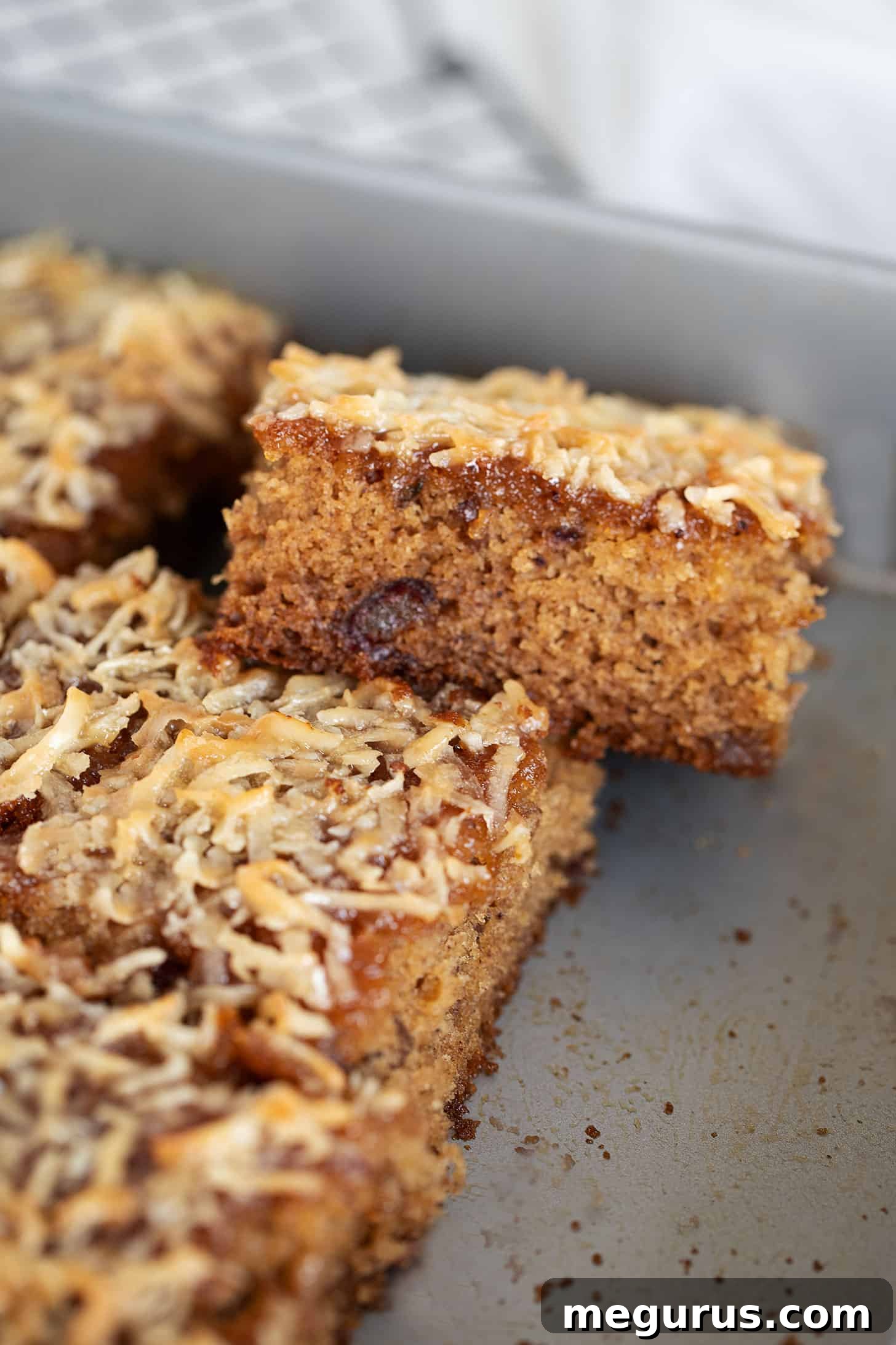 Close-up of a Queen Elizabeth Cake slice, showcasing the moist date interior and crunchy, golden coconut topping