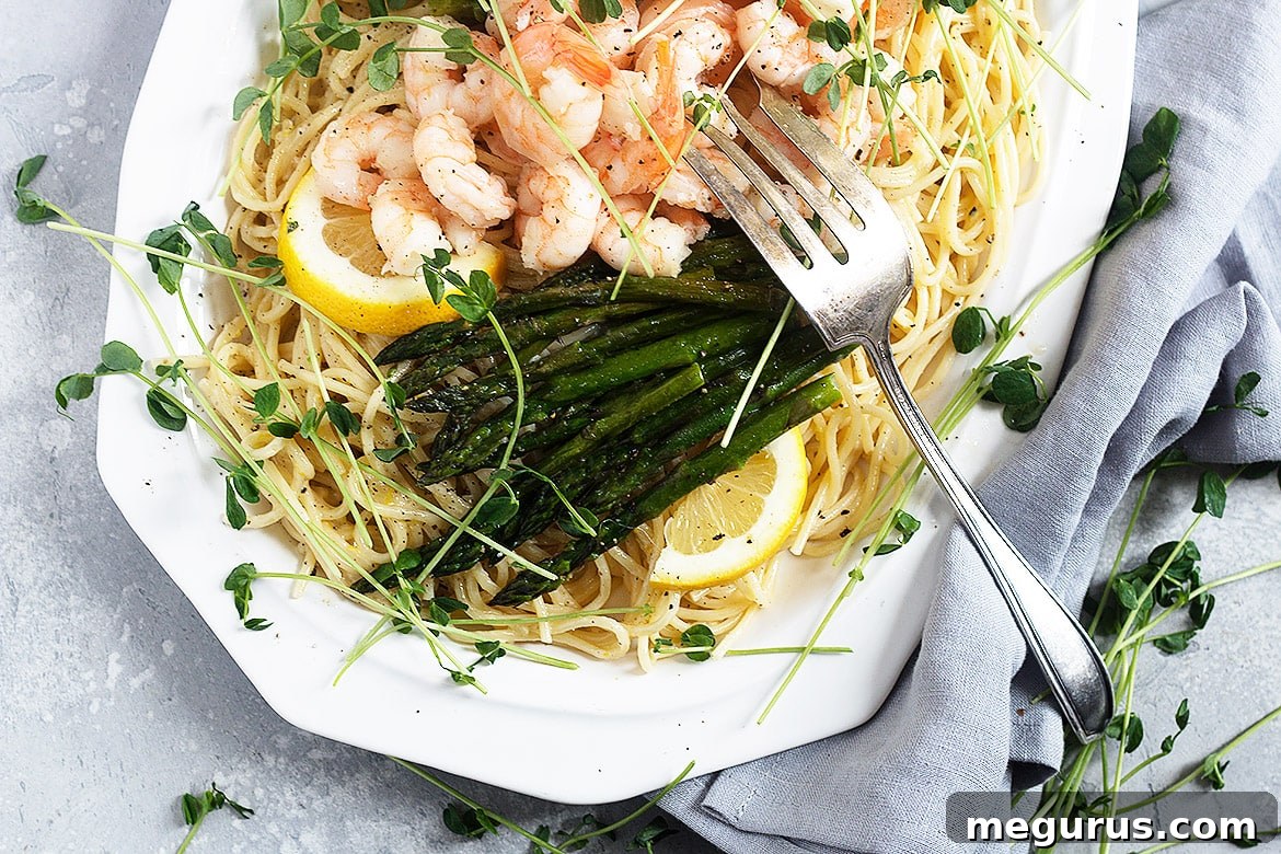 A close-up shot of creamy shrimp asparagus pasta on a white plate with a fork, garnished with fresh lemon.