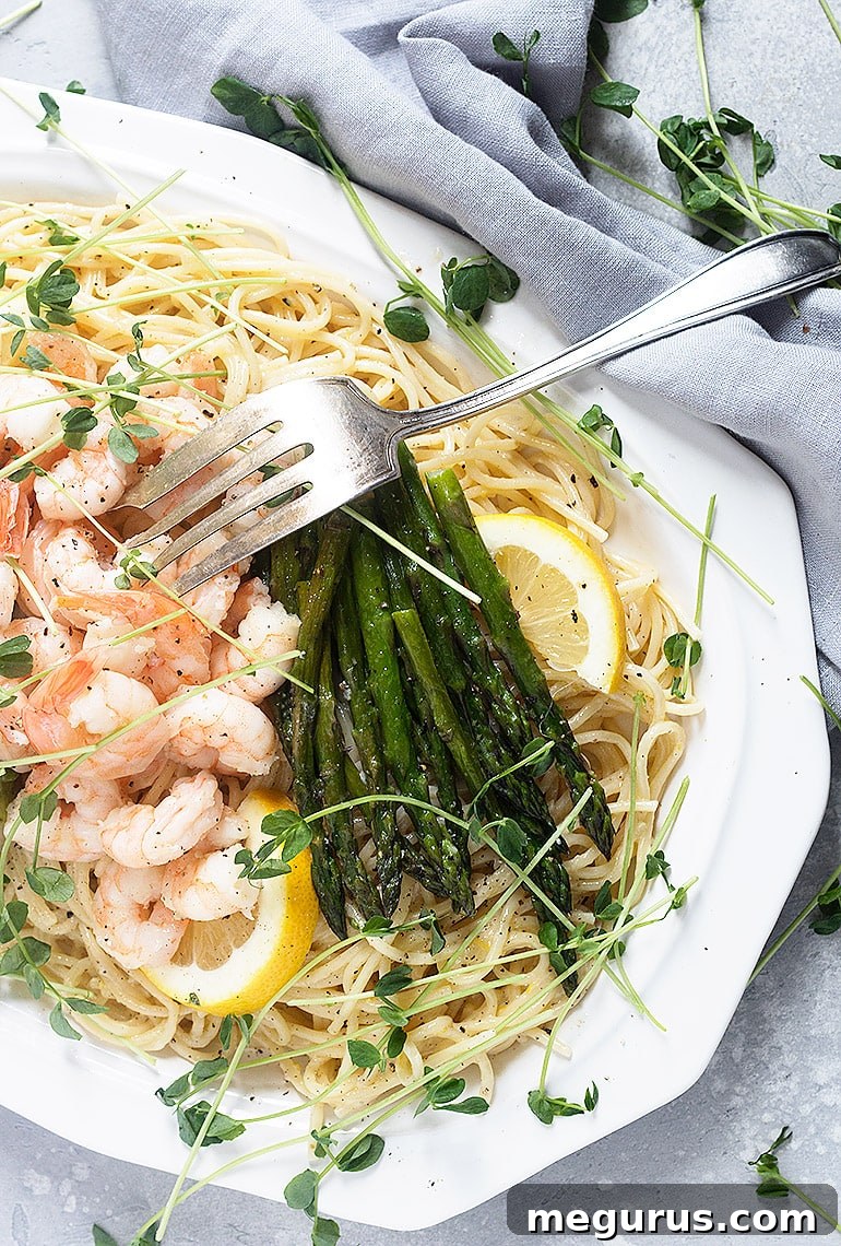 A vibrant lemon pasta dish with asparagus and shrimp, garnished with fresh herbs and lemon slices.