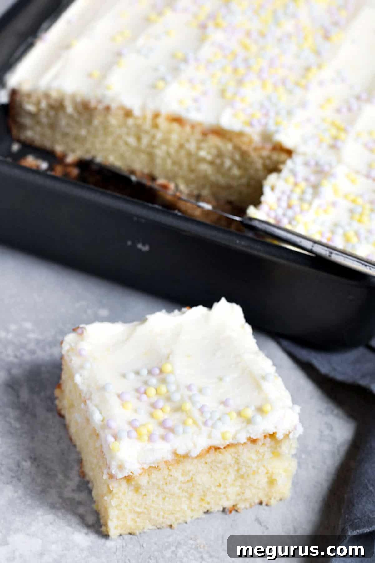 A close-up view of the perfectly frosted lemon sheet cake, showing the rich texture of the buttercream and the clean cut of a missing slice.