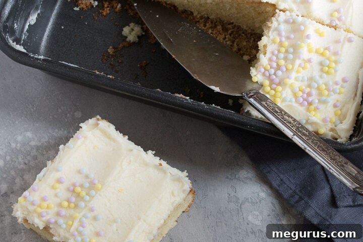 A slice of lemon sheet cake, showing the fluffy cake and creamy frosting, in a baking pan.