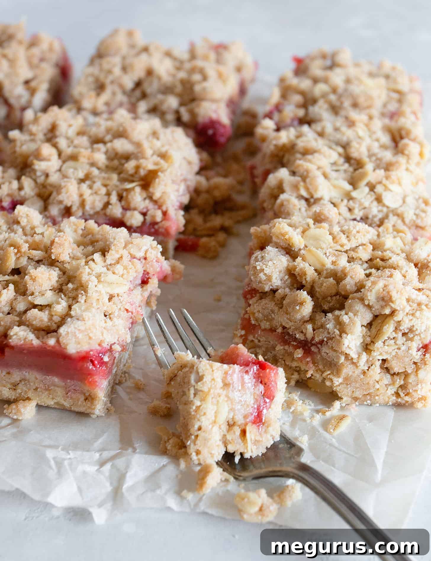 Individual strawberry rhubarb squares neatly cut and arranged on parchment paper.