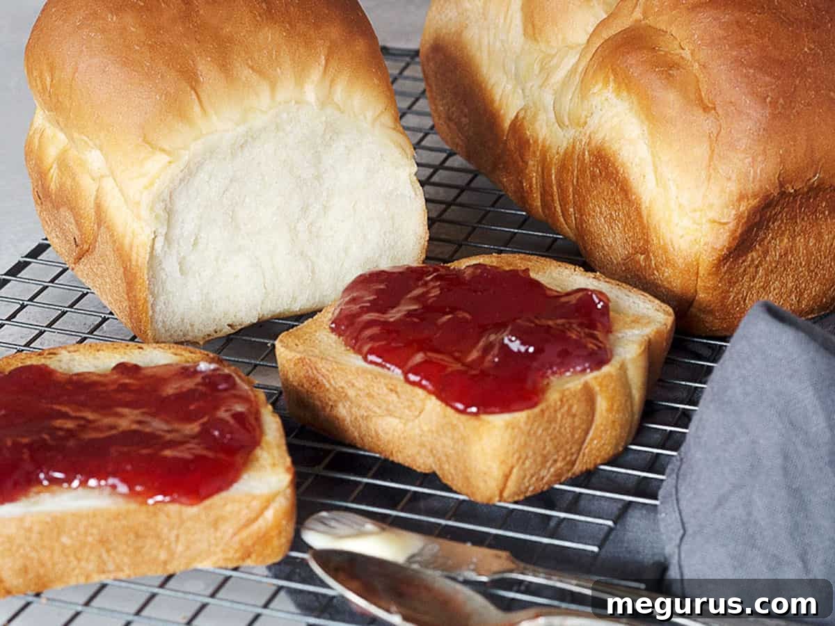Two loaves of freshly baked Shokupan, accompanied by slices of toasted bread and a jar of jam, showcasing its versatility for breakfast and beyond.
