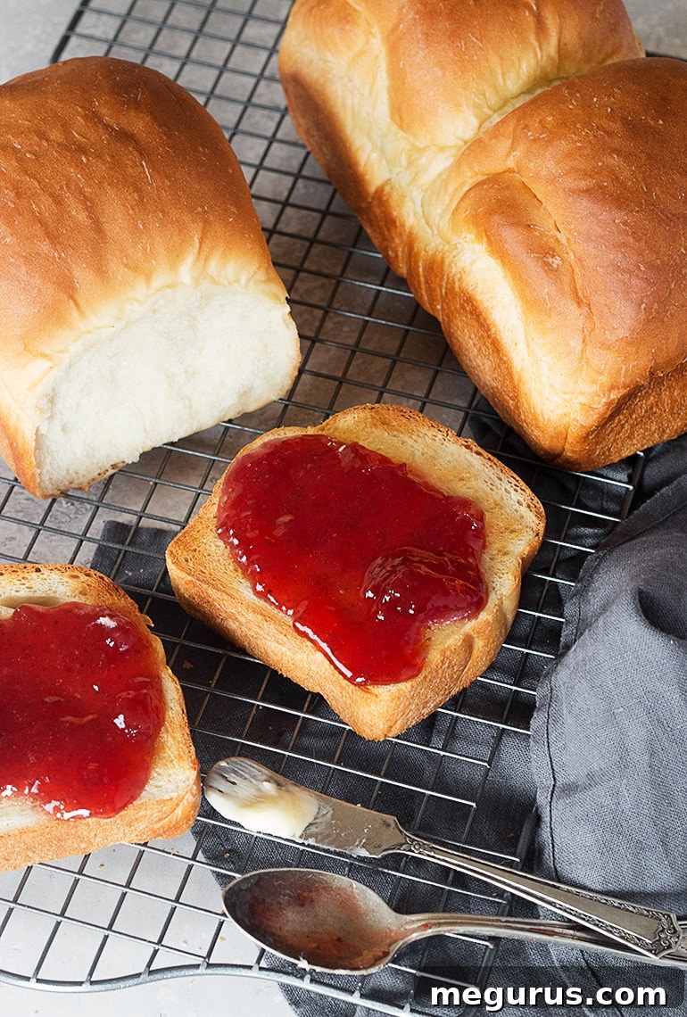Freshly baked Shokupan loaves cooling on a rack, with a side of toasted slices and jam, illustrating its perfect texture and serving suggestions.