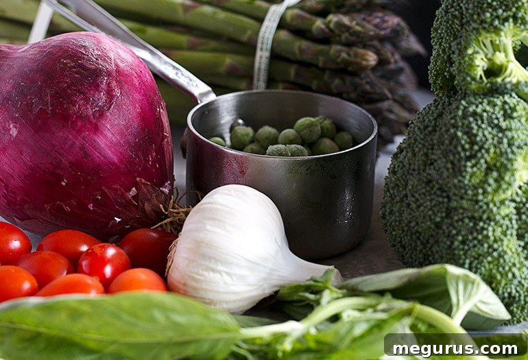 Fresh ingredients for Pasta Primavera laid out on a kitchen counter, including various vegetables, herbs, and pasta.