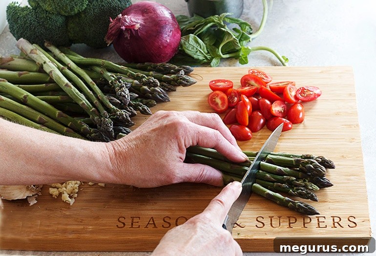 Hands preparing fresh vegetables for Pasta Primavera on a wooden cutting board, slicing and chopping various produce.