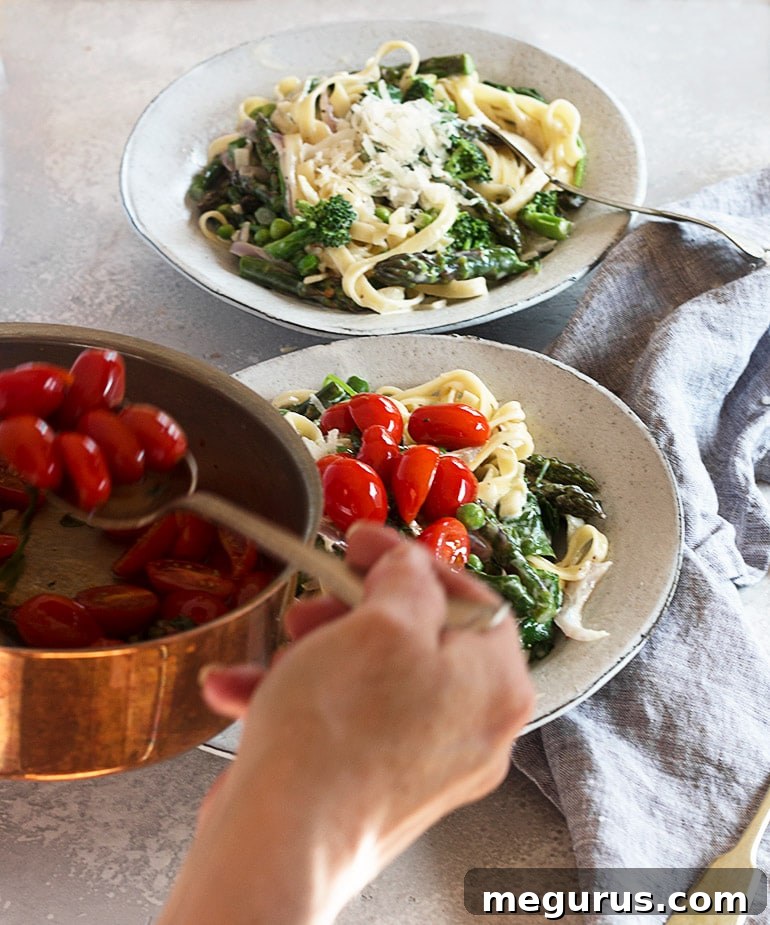 Warmed cherry tomatoes, basil, and garlic being spooned over a bowl of freshly prepared Pasta Primavera.