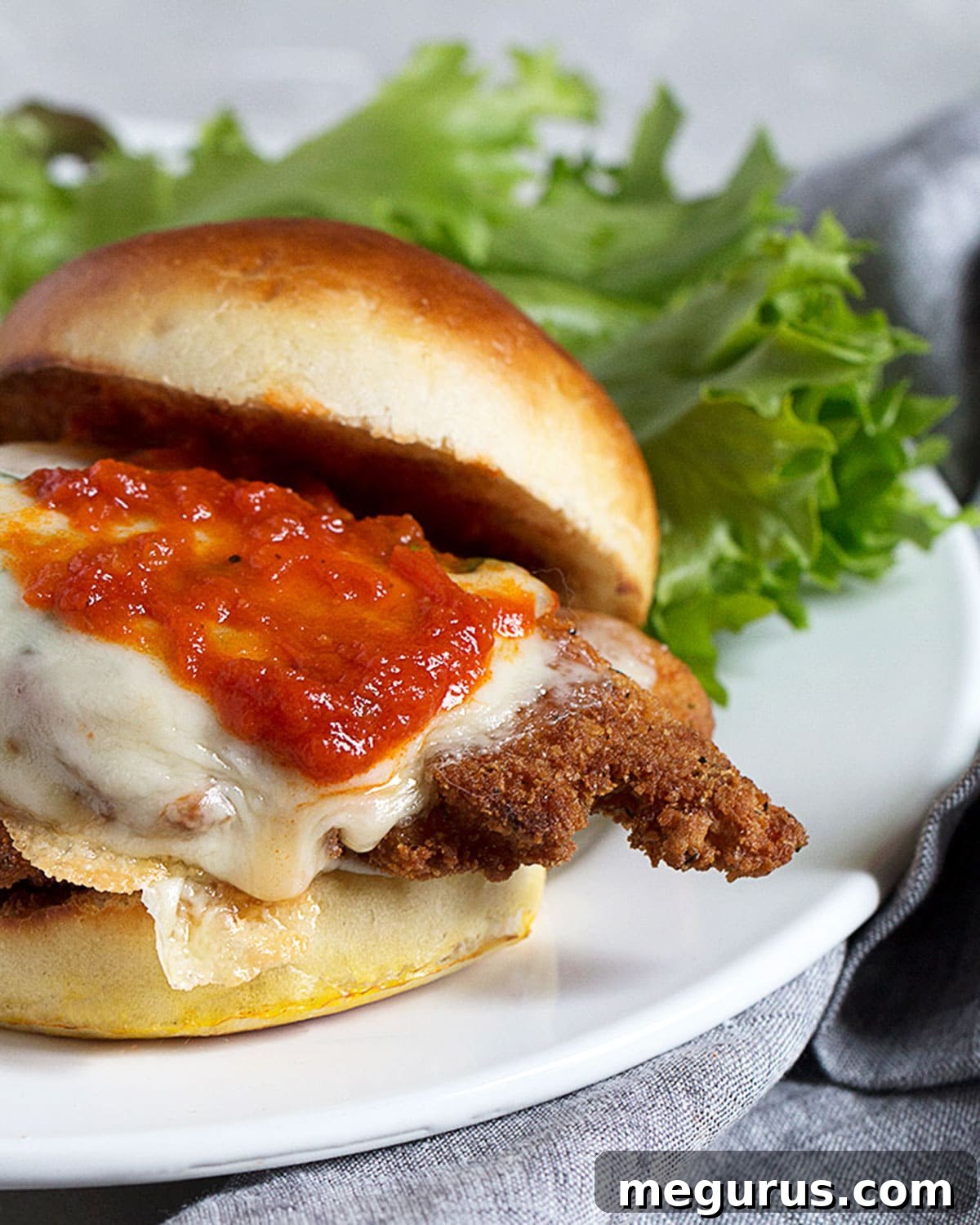 chicken parmesan on a bun on plate with lettuce