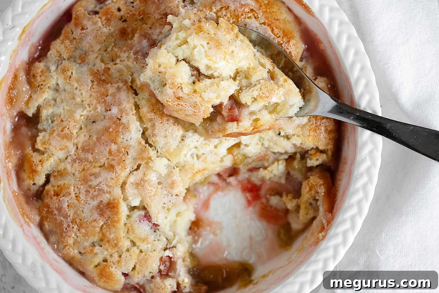 Rhubarb pudding cake in baking dish with spoon.