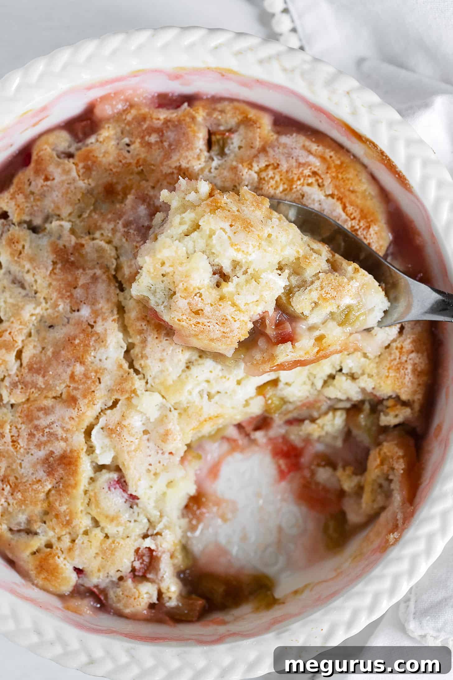 Rhubarb pudding cake in baking dish with spoon.