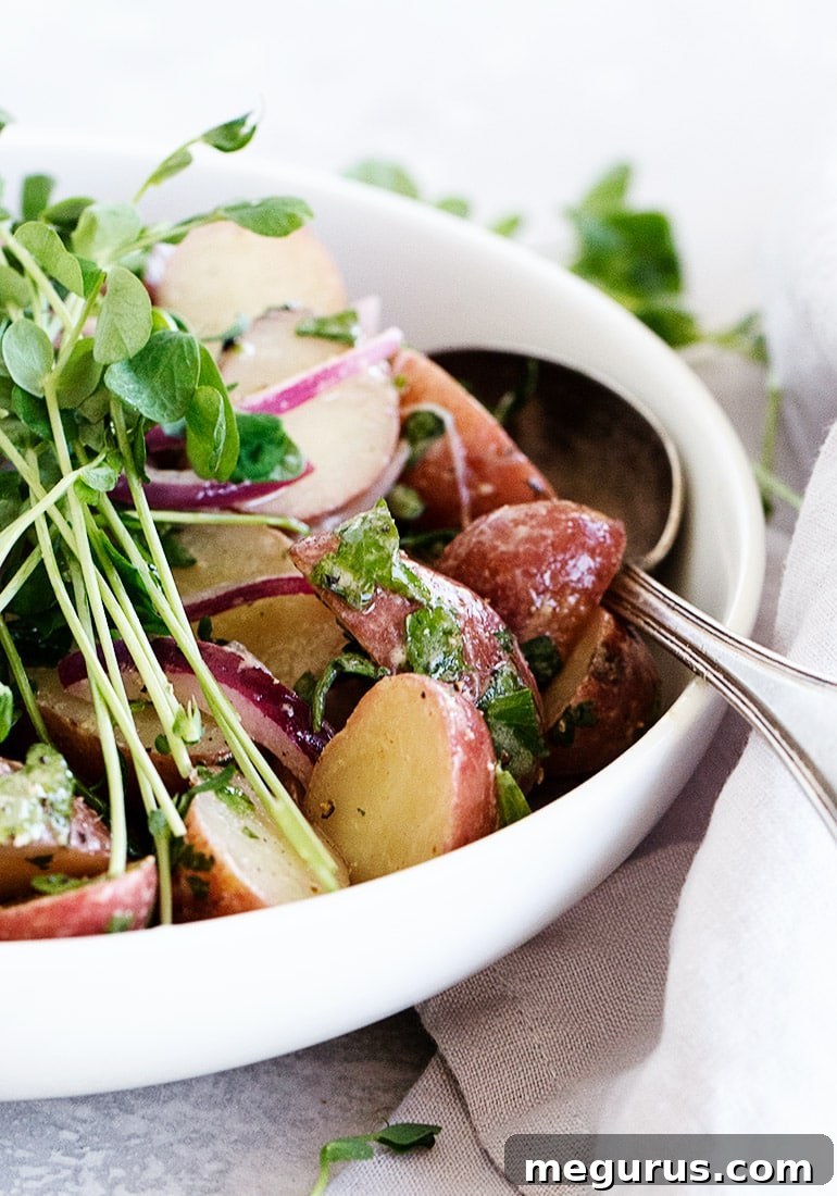 A close-up of a Dijon potato salad in a white serving bowl, showing the texture of potatoes, red onion, and fresh dill.