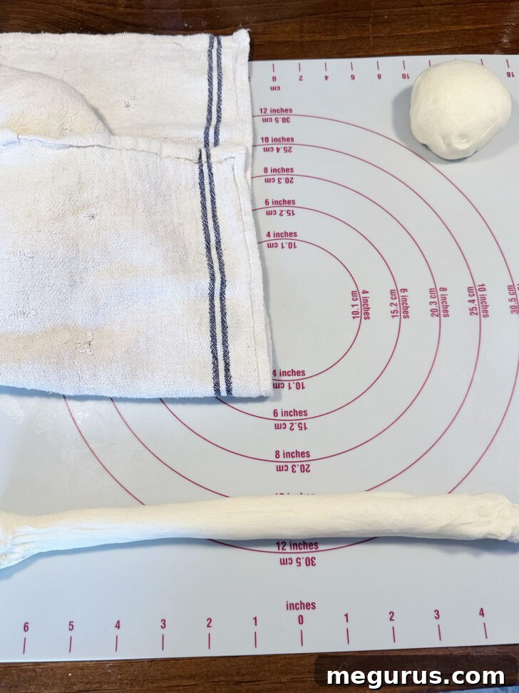 Hands rolling a dough rope from the center outwards, gradually lengthening it.