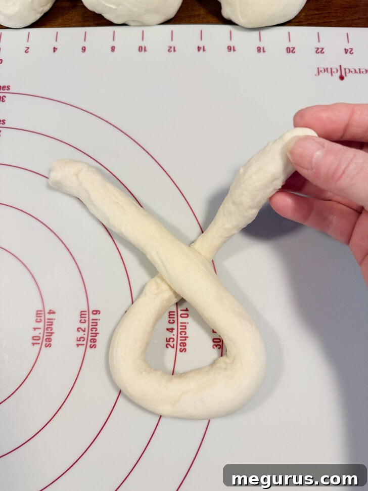 One strand of the crossed dough being folded down towards the bottom of the 'U'.