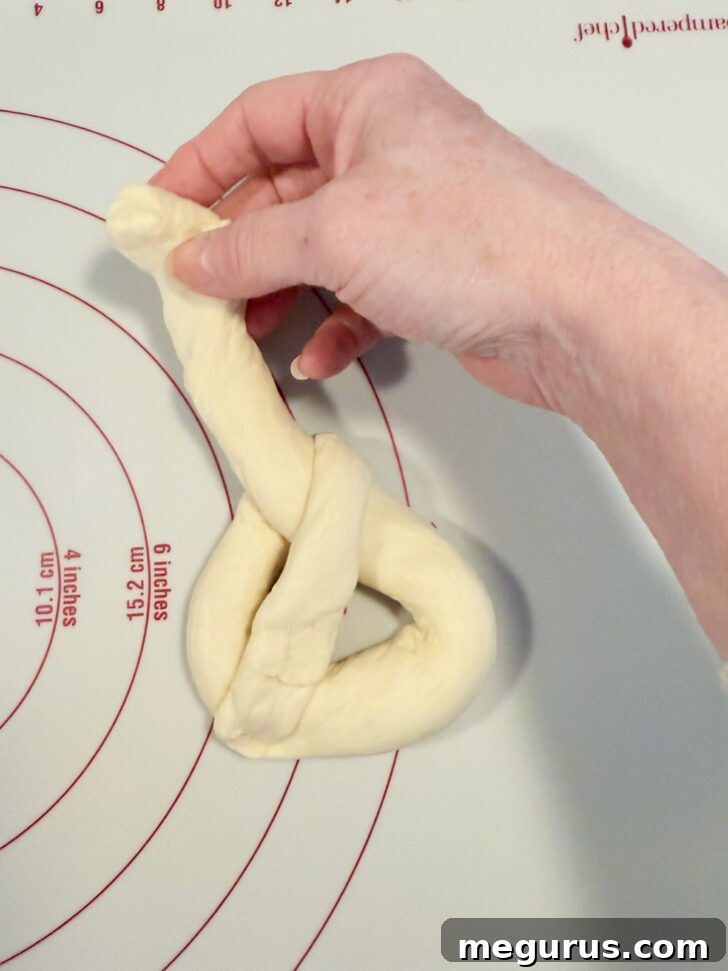 The second strand of dough being folded down and pinched to the bottom of the pretzel shape.