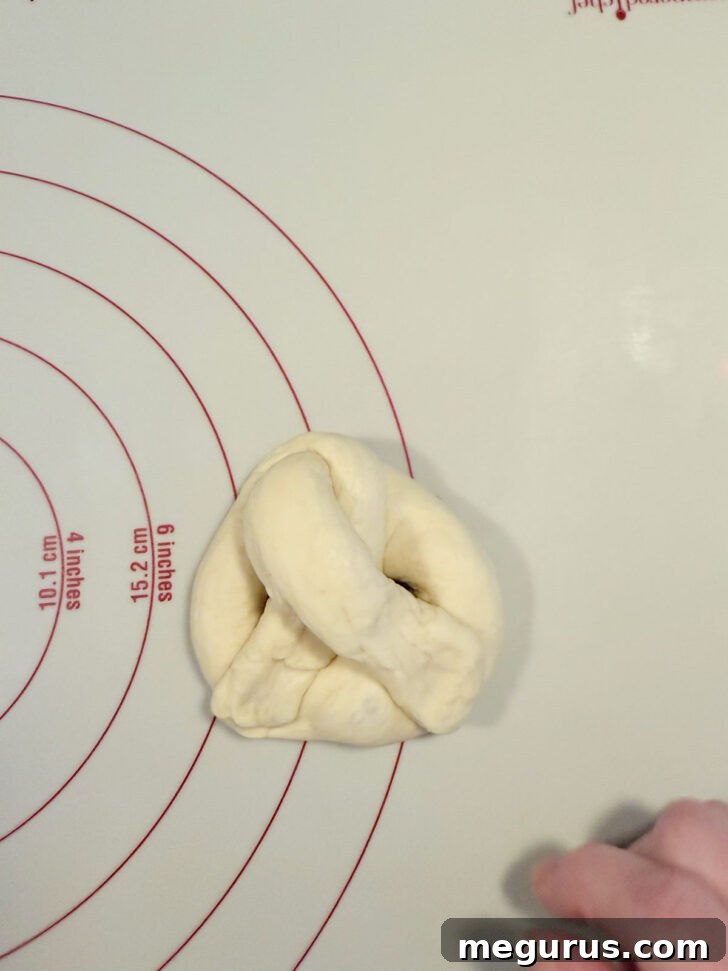 A freshly shaped pretzel on parchment paper, with its loops gently stretched.