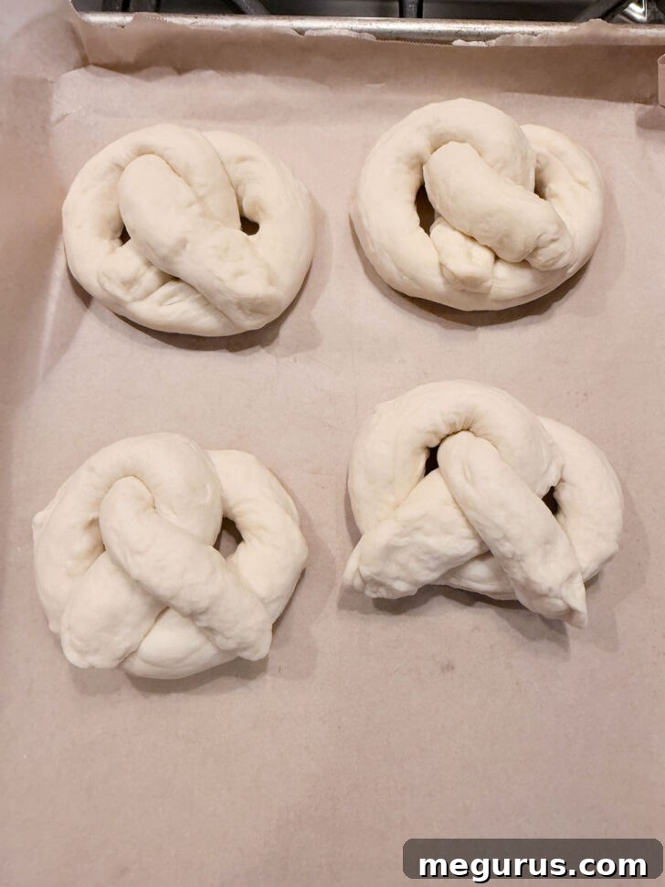 Multiple shaped pretzels laid out on a parchment-lined baking sheet, ready for boiling.