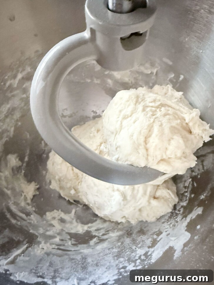 Pretzel dough in a stand mixer, with part of the flour incorporated, showing a slightly sticky texture.