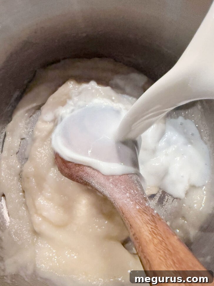 Milk being whisked into the beer and flour mixture in a saucepan to create a smooth sauce base.