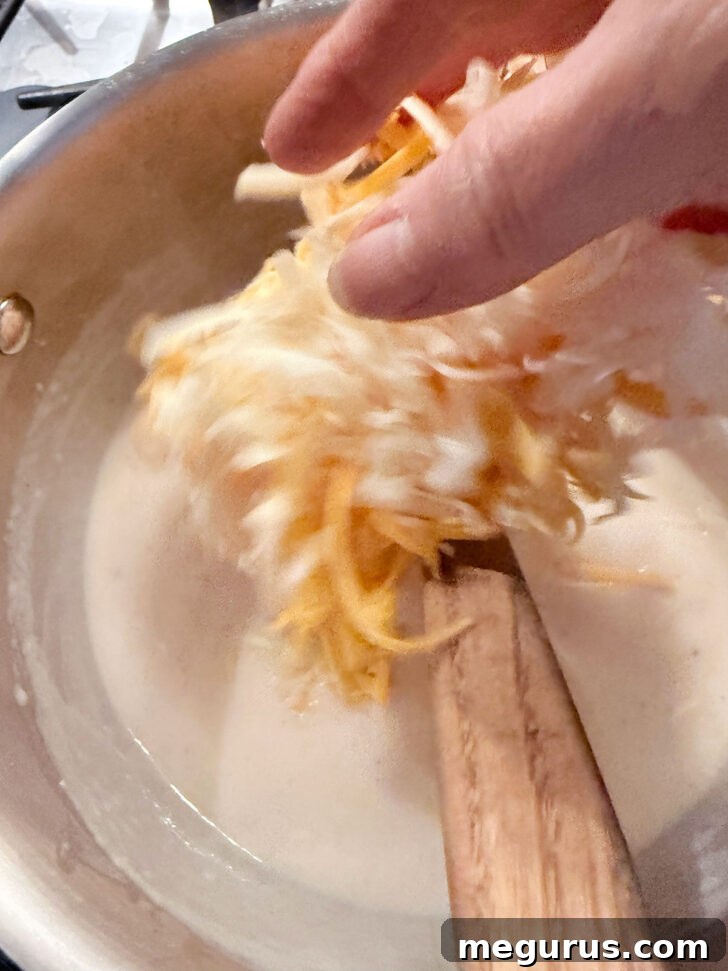 Shredded cheese being added to the saucepan off the heat, for a smooth melt.