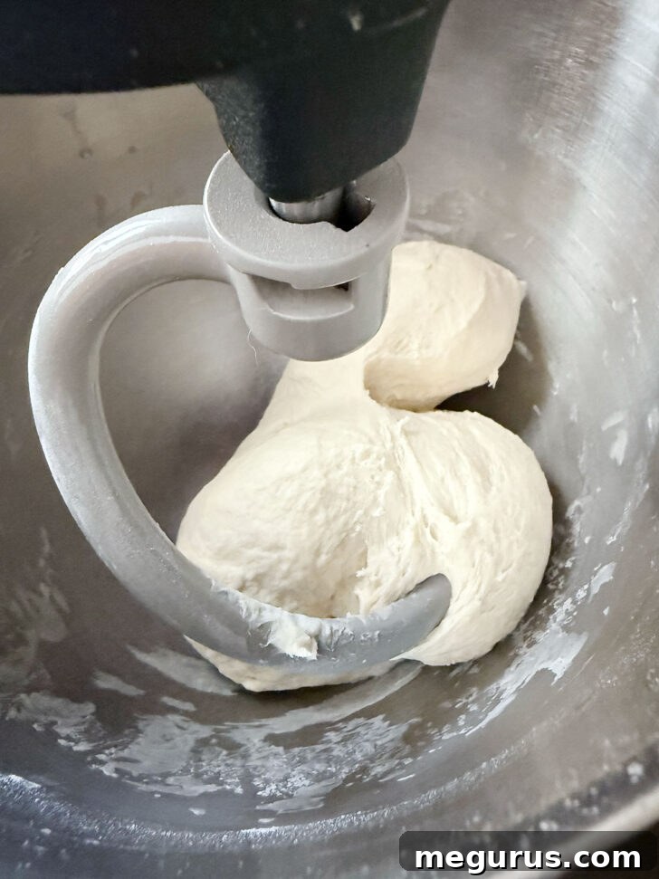 Fully kneaded pretzel dough in a stand mixer, clean from the bowl and wrapping around the hook.