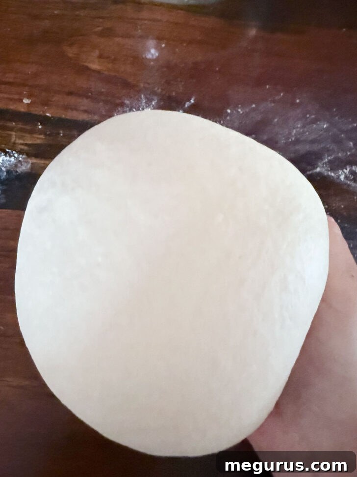 Smooth, rounded ball of pretzel dough on a lightly floured surface after kneading.