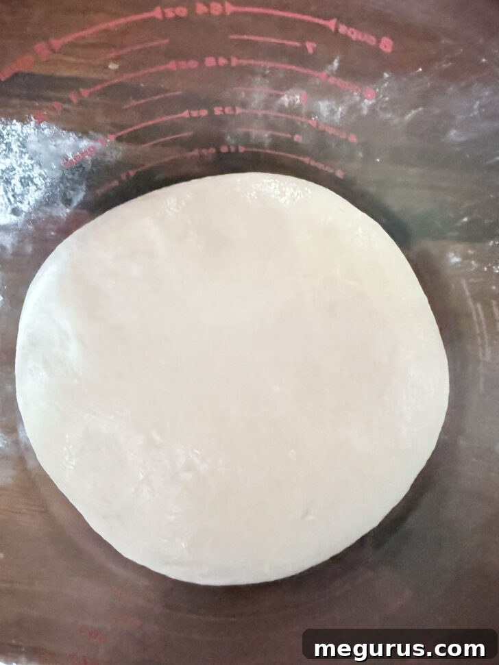 Smooth dough ball resting in a large greased measuring cup, ready for its first rise.