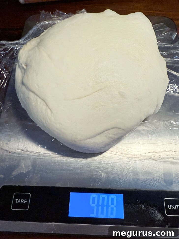 Pretzel dough ball being weighed on a digital kitchen scale for accurate portioning.