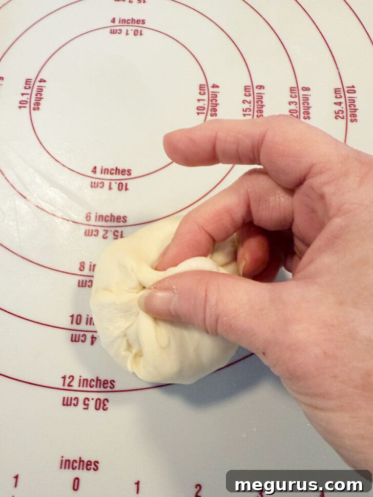Hand shaping a small piece of dough into a smooth, round ball.