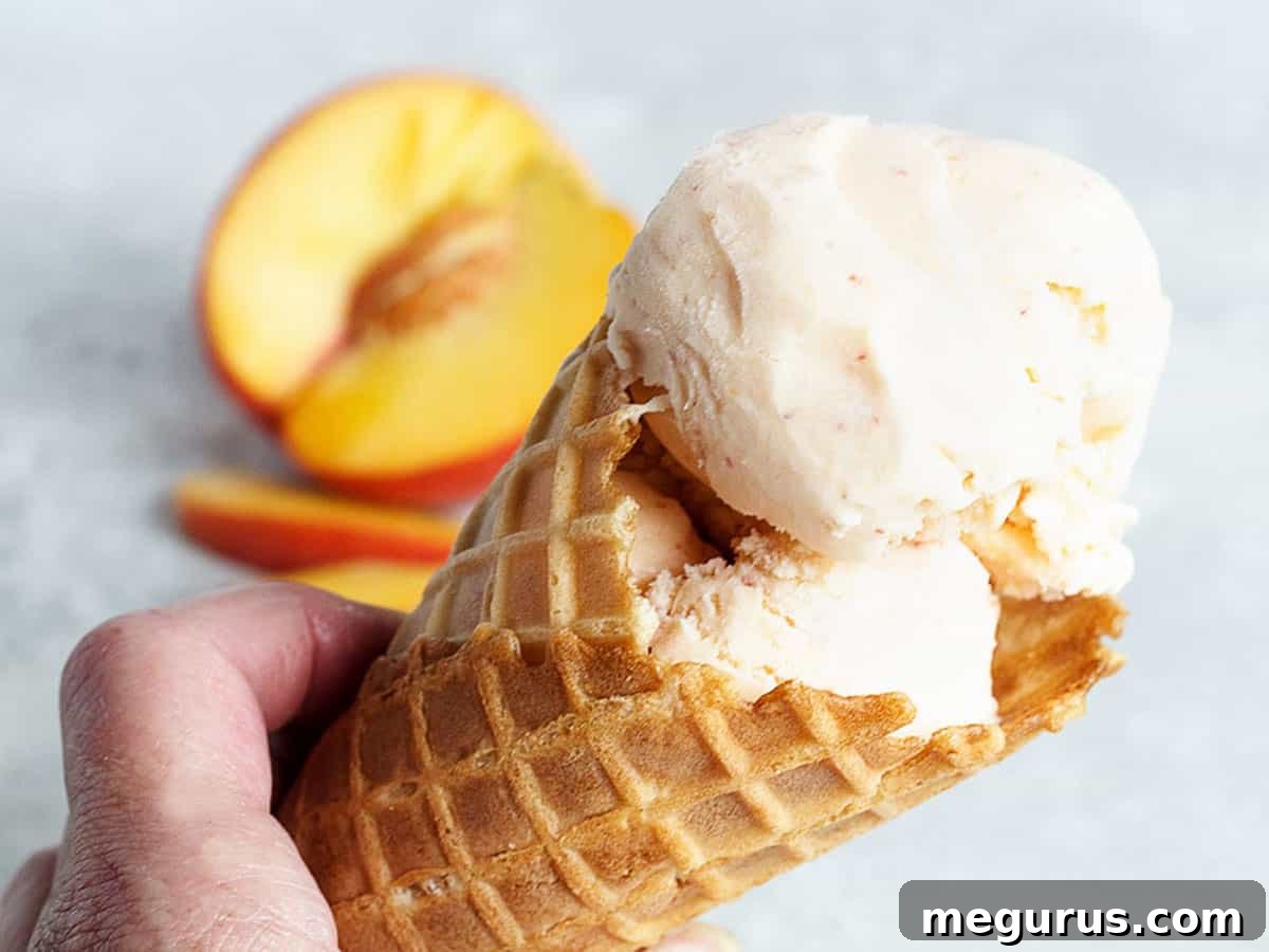 Fresh peach ice cream in a waffle cone, garnished with a peach slice, evoking summer flavors.