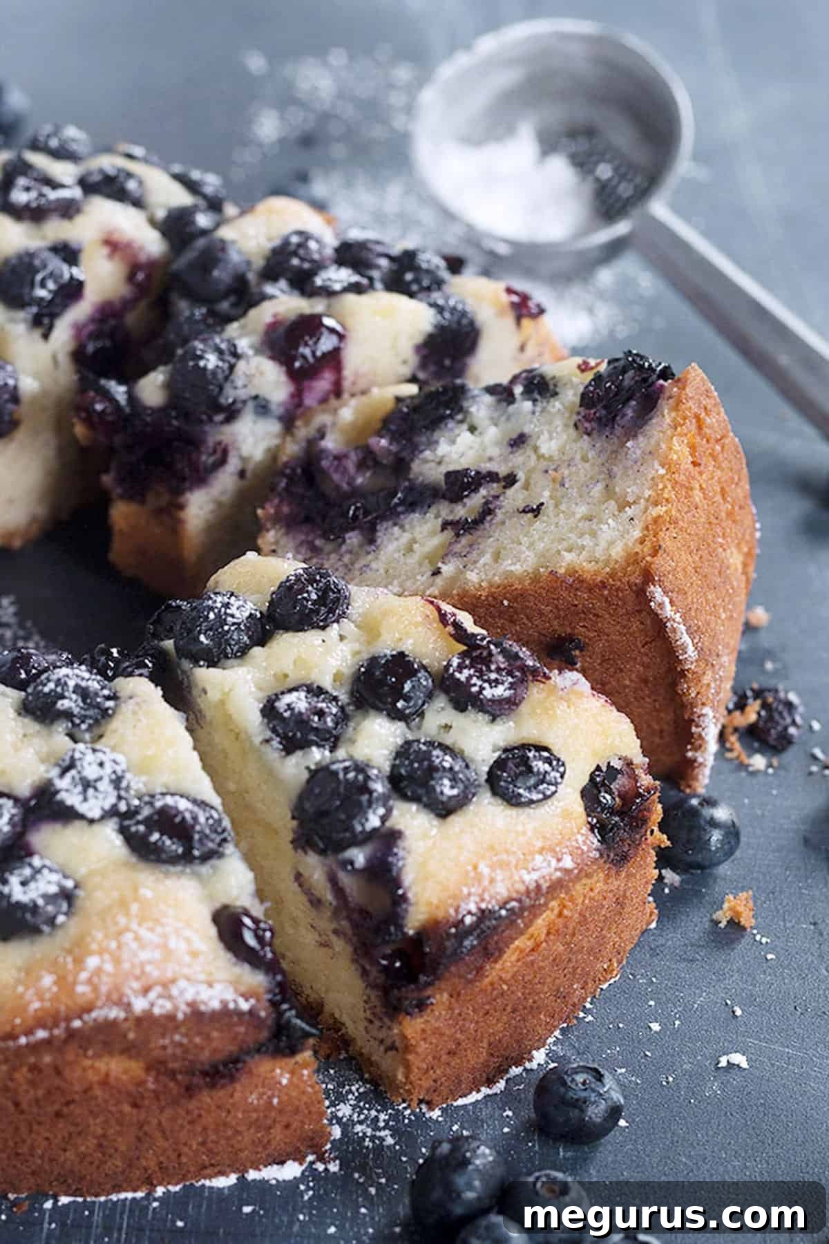 Close-up of a slice of moist blueberry sour cream cake on a blue background, dusted with powdered sugar
