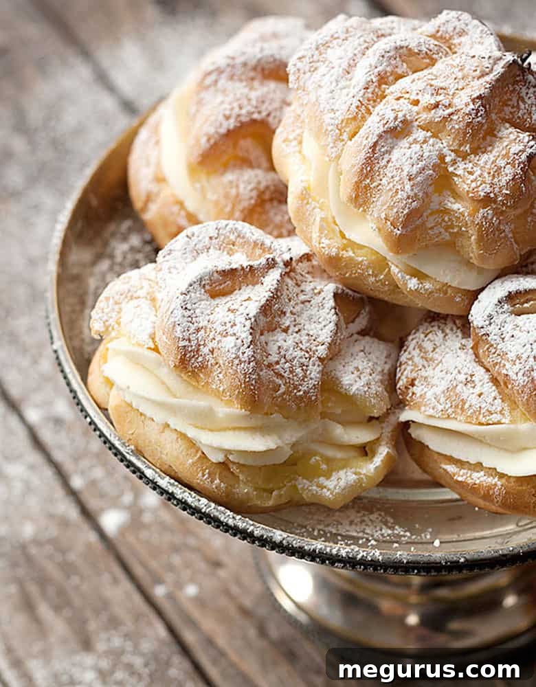 Close-up of a single golden-brown cannoli cream filled cream puff, delicately dusted with icing sugar on a silver stand.