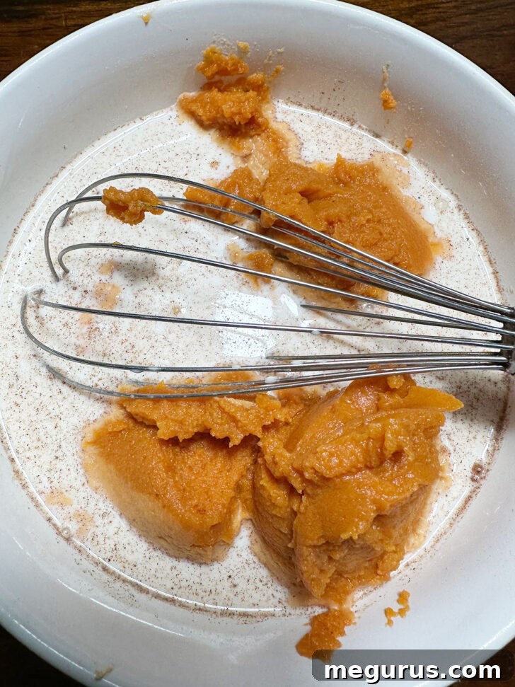 Adding evaporated milk, whole milk, and pumpkin puree to the bowl of dry ingredients.