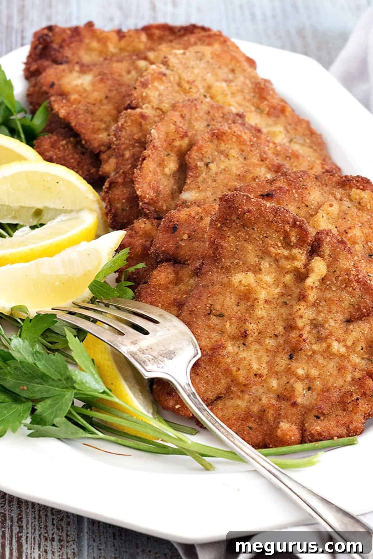 Two pieces of perfectly cooked golden-brown pork schnitzel on a white plate, garnished with fresh lemon wedges.