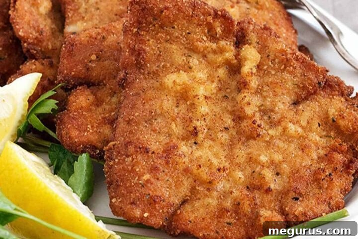 A close-up of a perfectly fried pork schnitzel, garnished with a fresh lemon slice and a sprig of parsley.