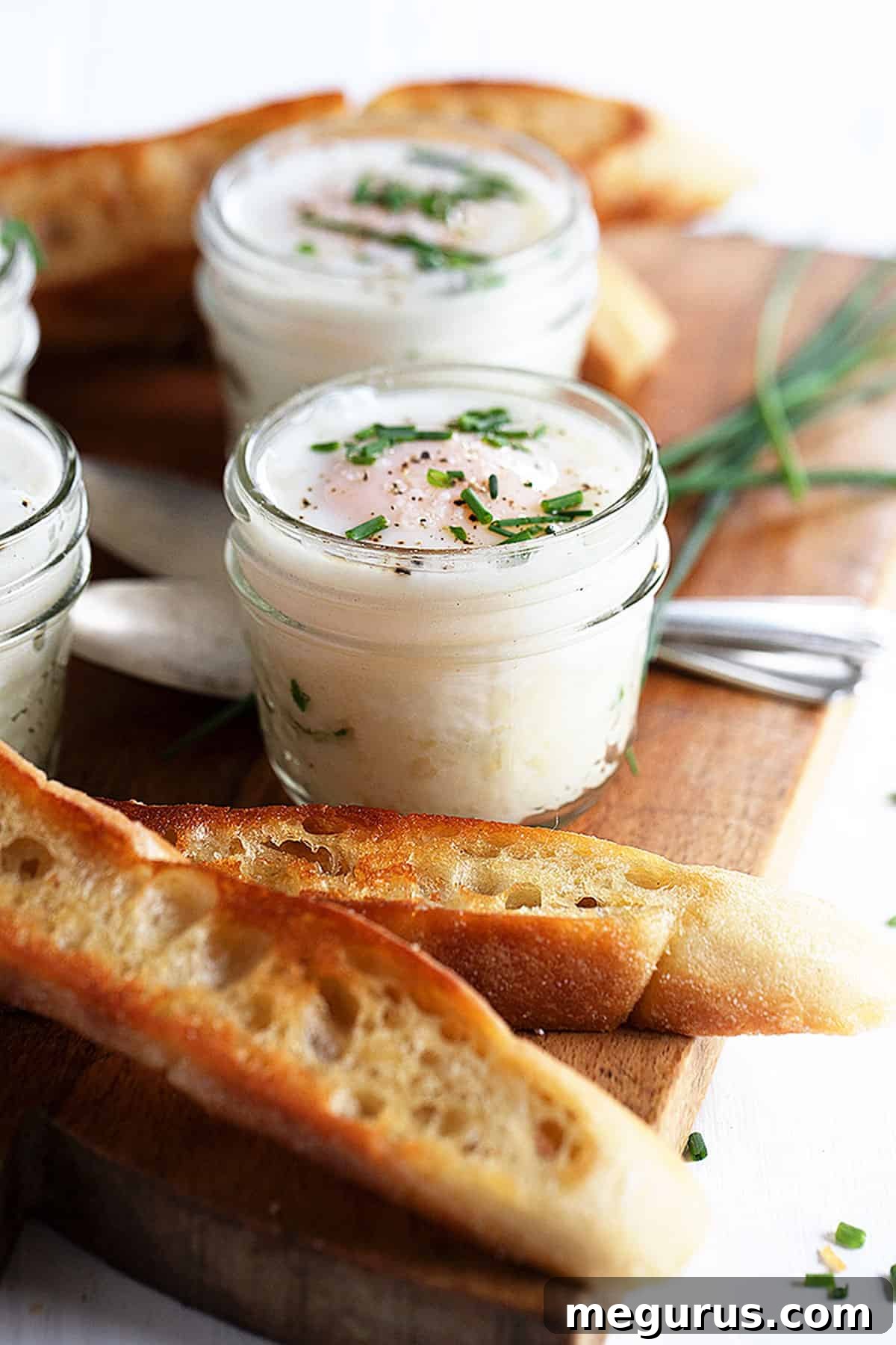 Close-up of coddled eggs in small jars with mashed potatoes, garnished with chives.