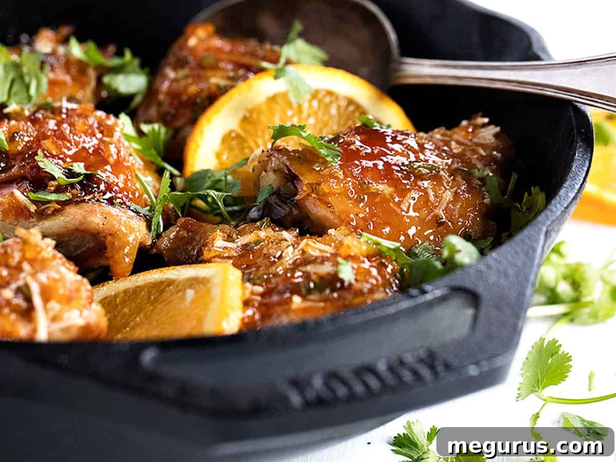 sticky orange chicken in skillet with orange slices, showcasing a perfectly glazed dish