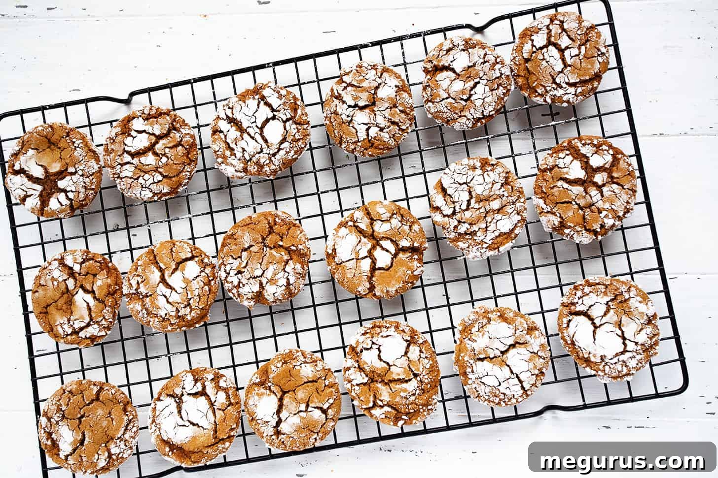 Freshly baked ginger crackle cookies cooling on a wire rack, dusted with powdered sugar.