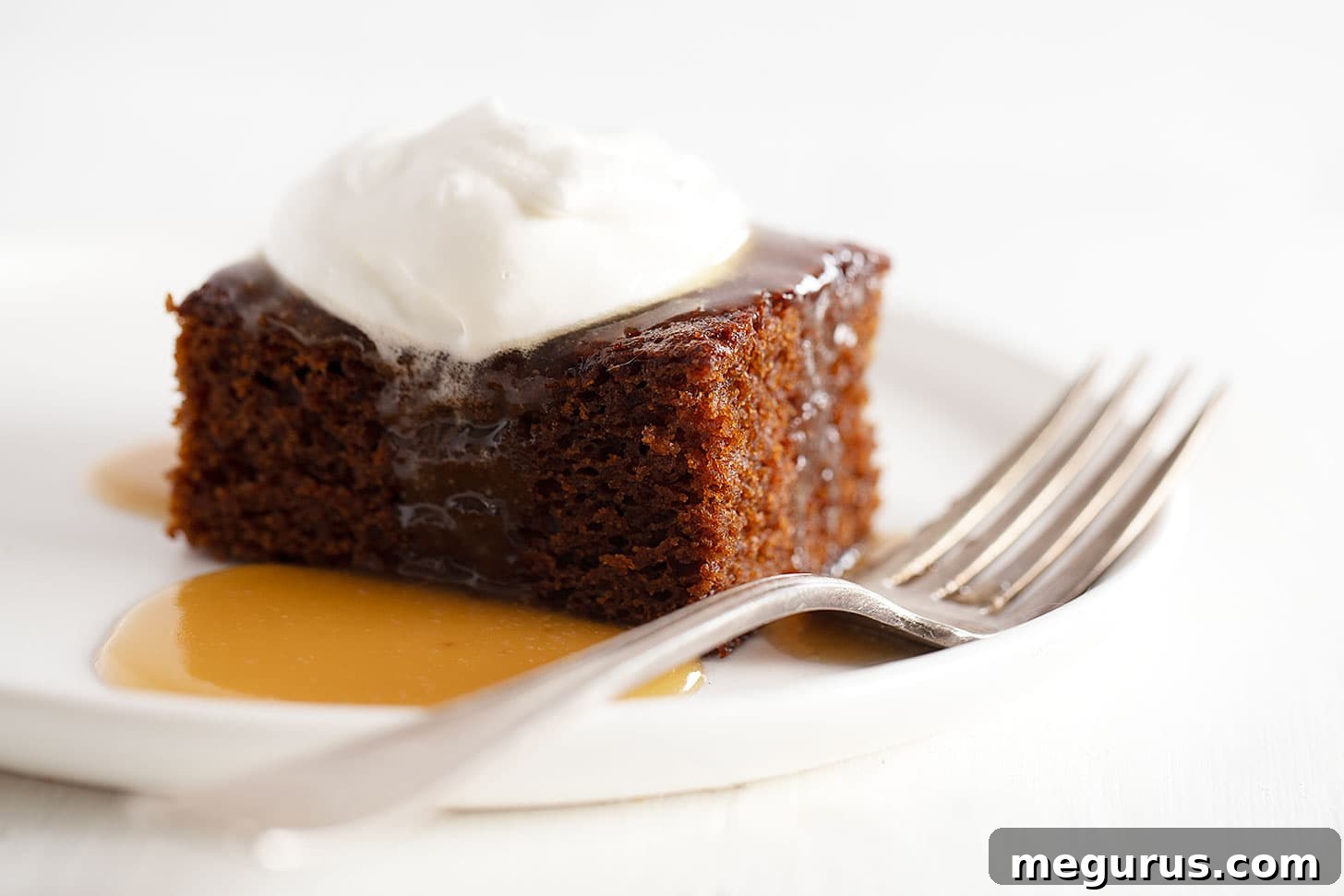Classic Gingerbread Cake with warm caramel sauce and whipped cream on a plate, ready to be enjoyed as a festive holiday dessert.