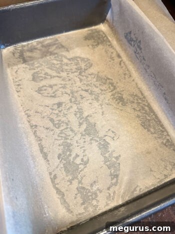 A baking pan meticulously lined with parchment paper, extending over the sides for easy cake removal after baking.