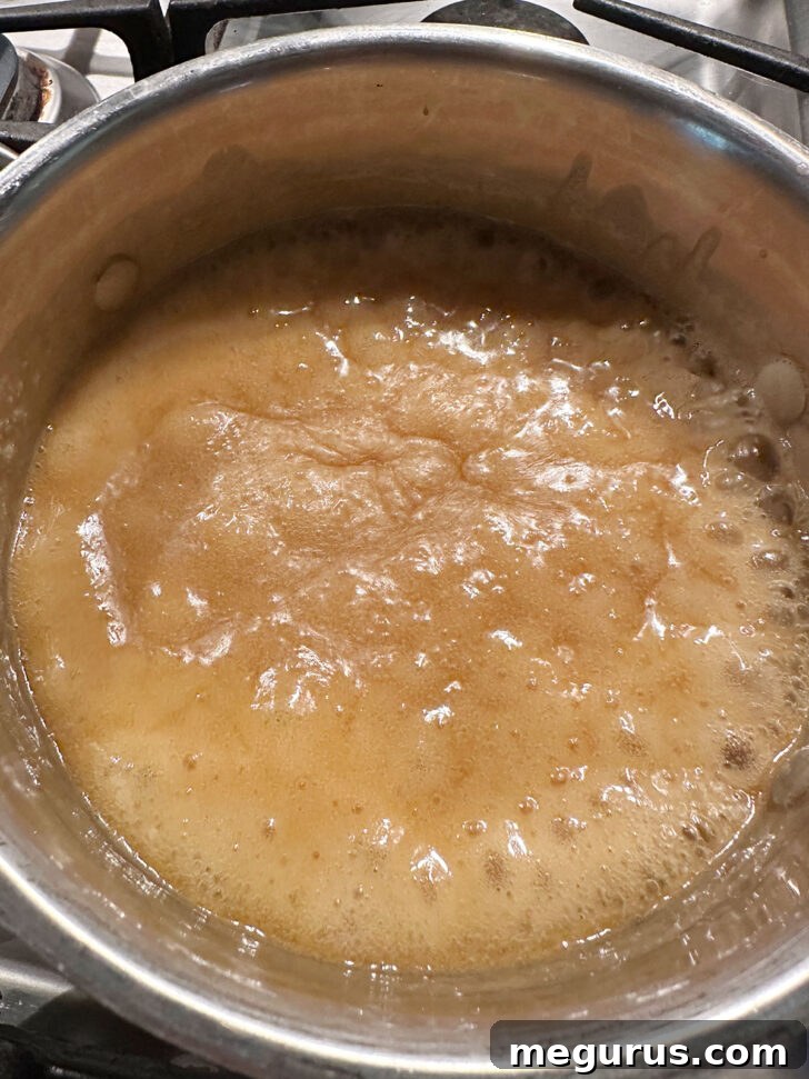 The caramel sauce mixture vigorously boiling in a saucepan on the stovetop, developing its rich flavor and thick consistency.