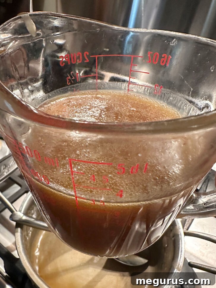 The finished, glossy caramel sauce poured into a clear glass measuring cup, showcasing its golden-brown color and smooth texture.