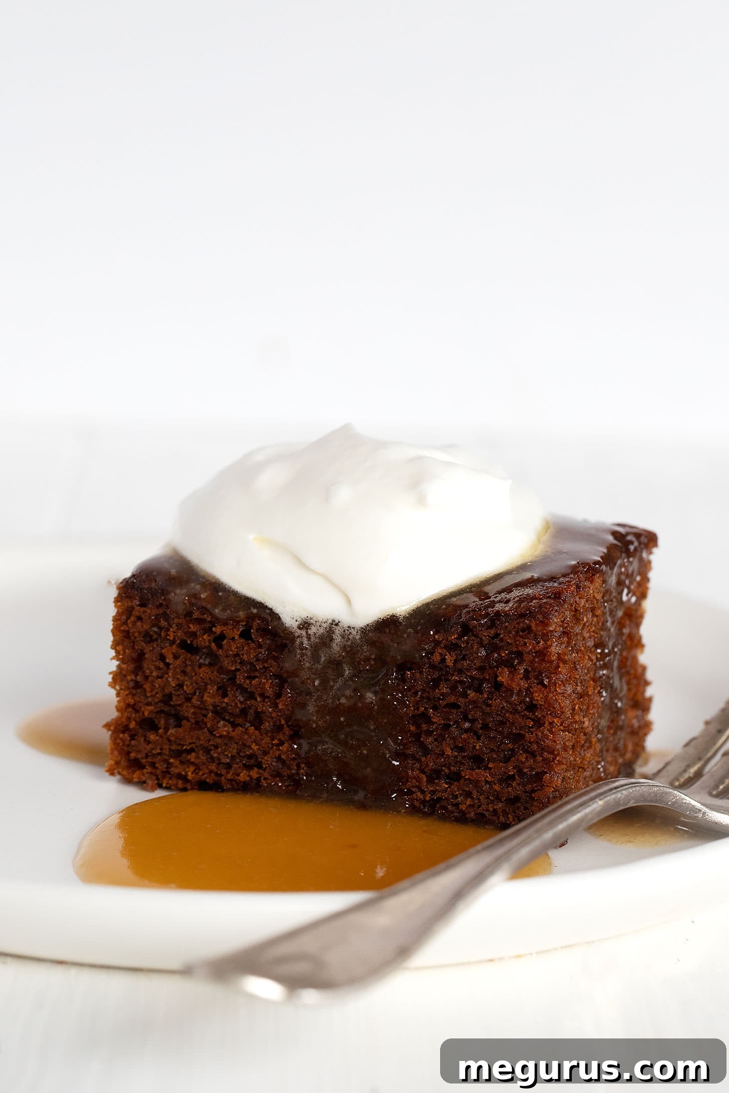 A beautifully plated slice of classic gingerbread cake, topped with a generous pour of warm caramel sauce and a dollop of fresh whipped cream, ready to be served.