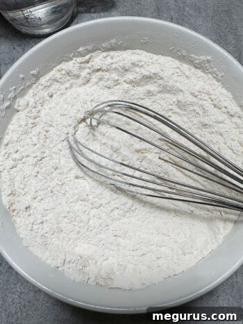 Whisking together the dry ingredients—flour, baking powder, and ground ginger—in a large mixing bowl.