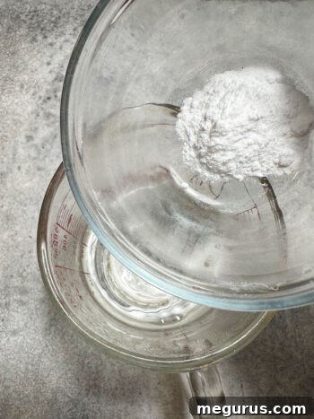 Dissolving baking soda into a cup of freshly boiled water, creating a fizzing mixture vital for the cake's rise and texture.