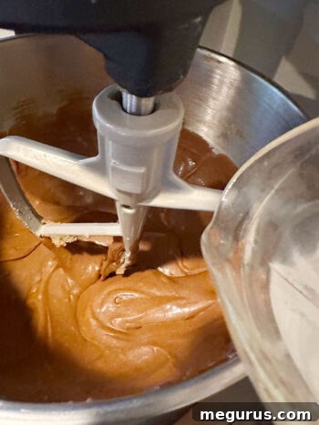 Pouring the hot baking soda water mixture into the molasses batter, stirring gently to combine the ingredients.