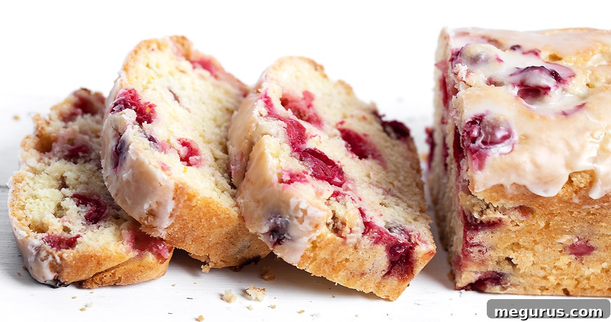 Sliced cranberry orange loaf cake on a white background, showcasing its moist texture and abundant cranberries