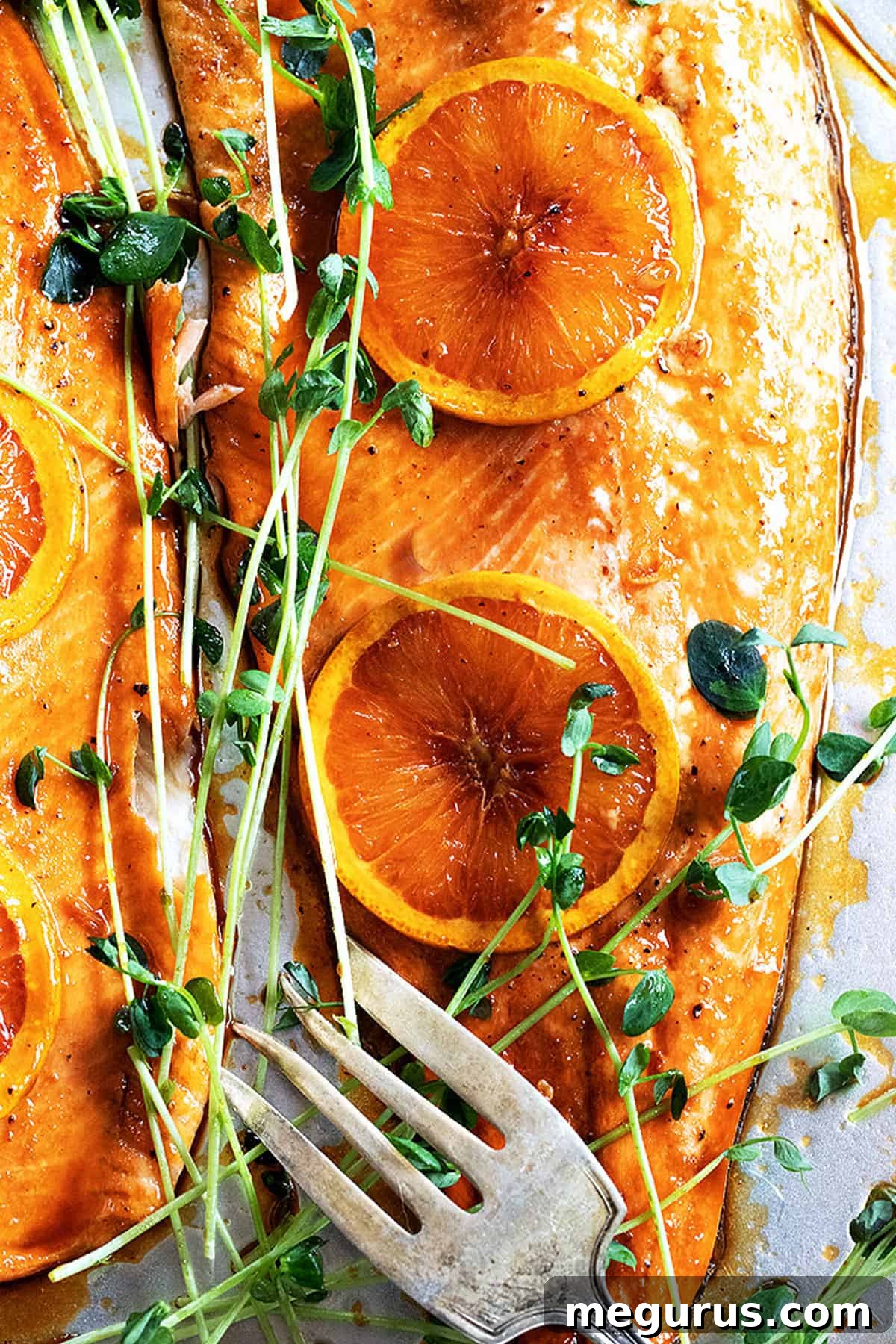 Perfectly cooked Asian orange salmon fillets on a baking sheet, garnished with fresh orange slices