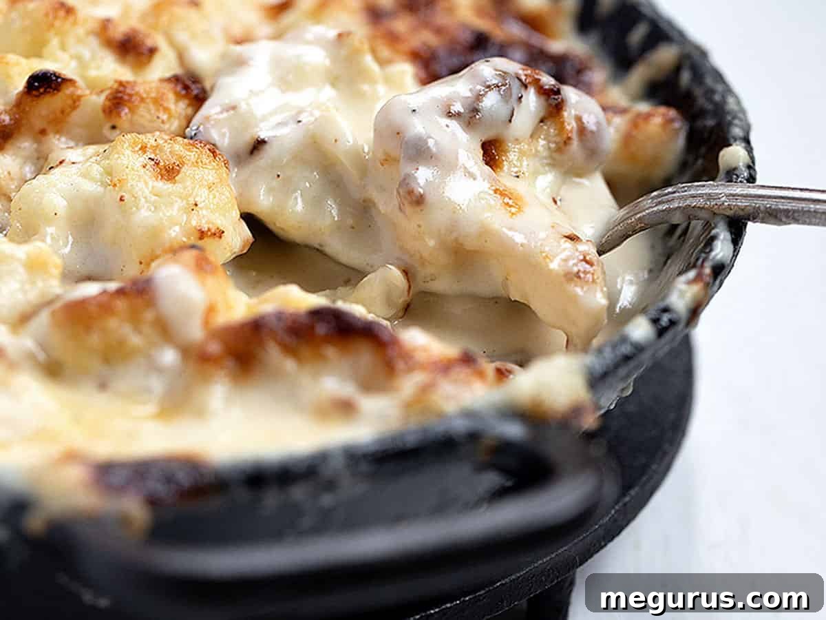 Golden brown roasted cauliflower cheese in a cast iron skillet with a serving spoon