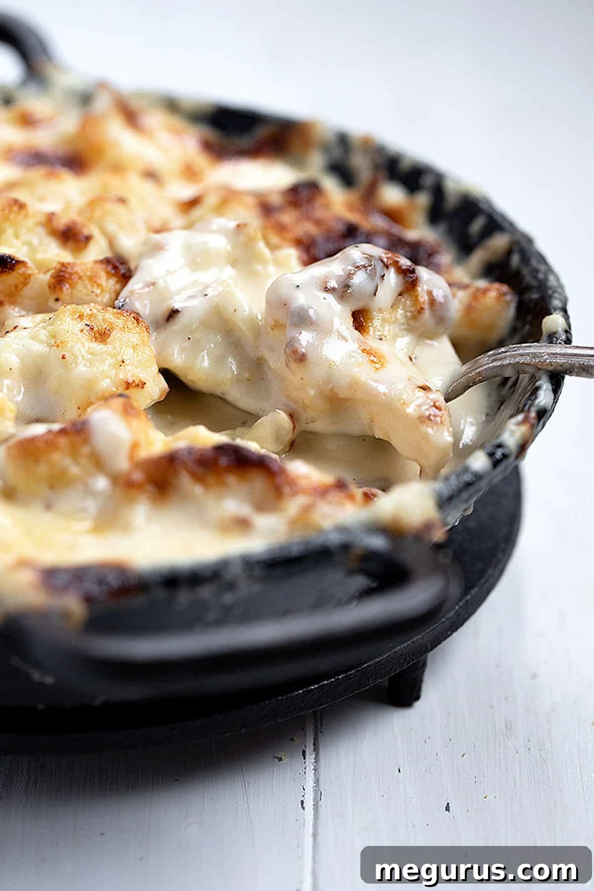 Close-up of baked cauliflower cheese, golden and bubbly, with a serving spoon
