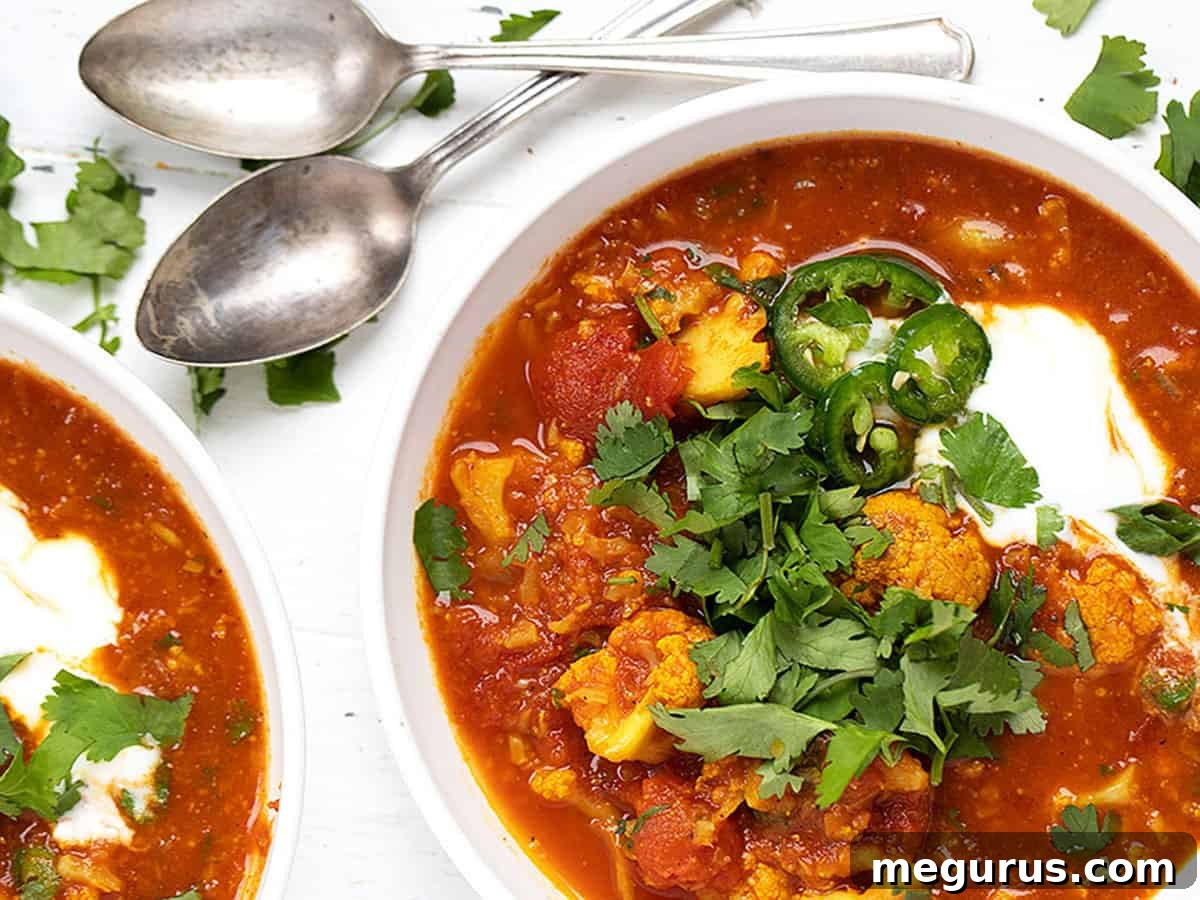 Indian spiced cauliflower soup in white bowls with spoons, garnished with fresh cilantro